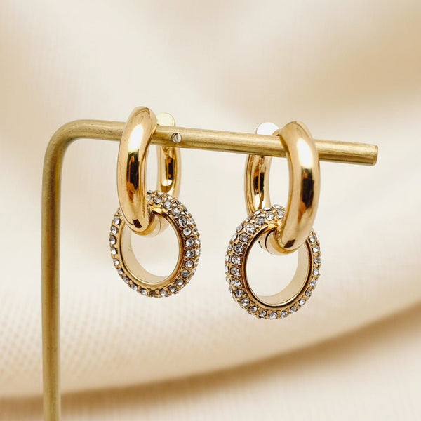 Gold pavé crystal huggie hoop earrings with a removable crystal circle drop on an ivory background