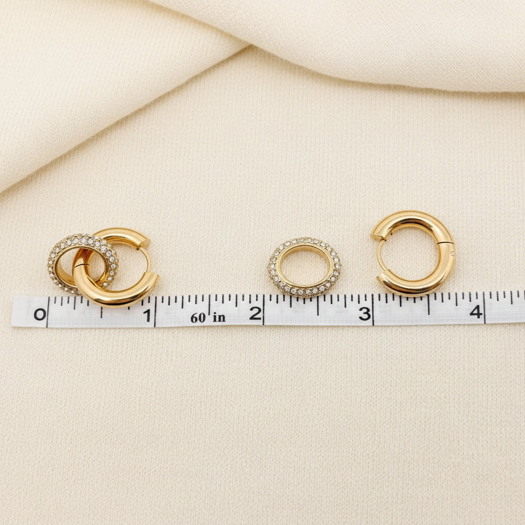 Three gold hoop earrings with a measuring tape for scale on an ivory background