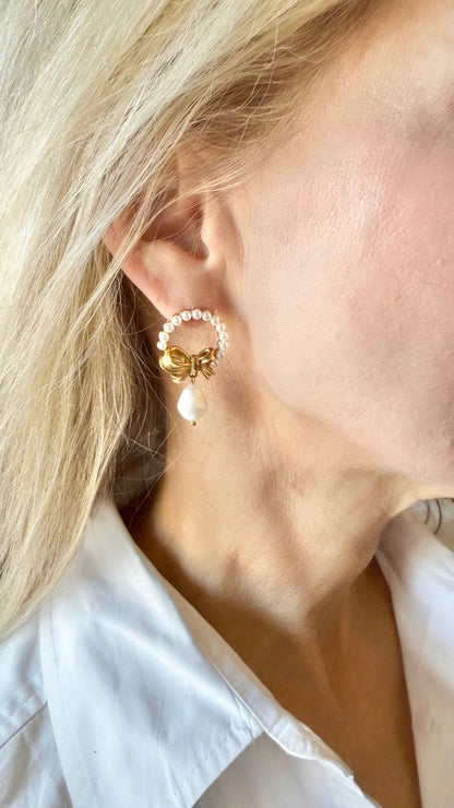 Close-up of a person wearing a gold bow and pearl wreath earring and a white shirt