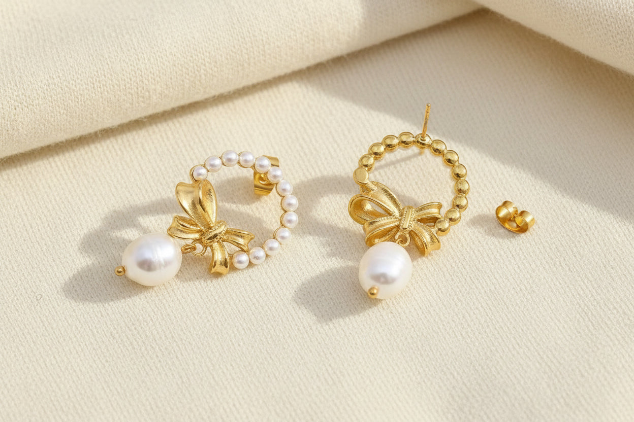 Gold bow and pearl wreath earrings with one showing the back post detail against a grey textured background