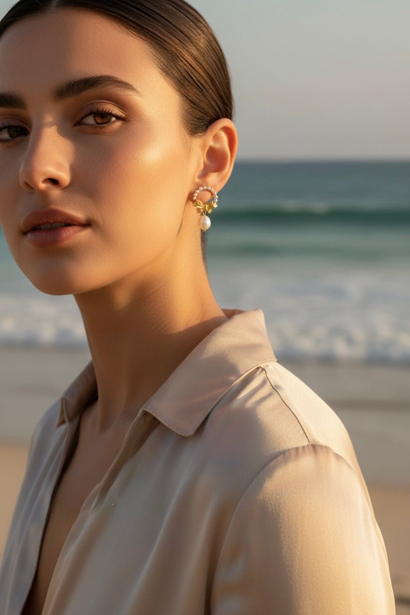 Woman wearing a gold bow and pearl wreath earring with a beach background