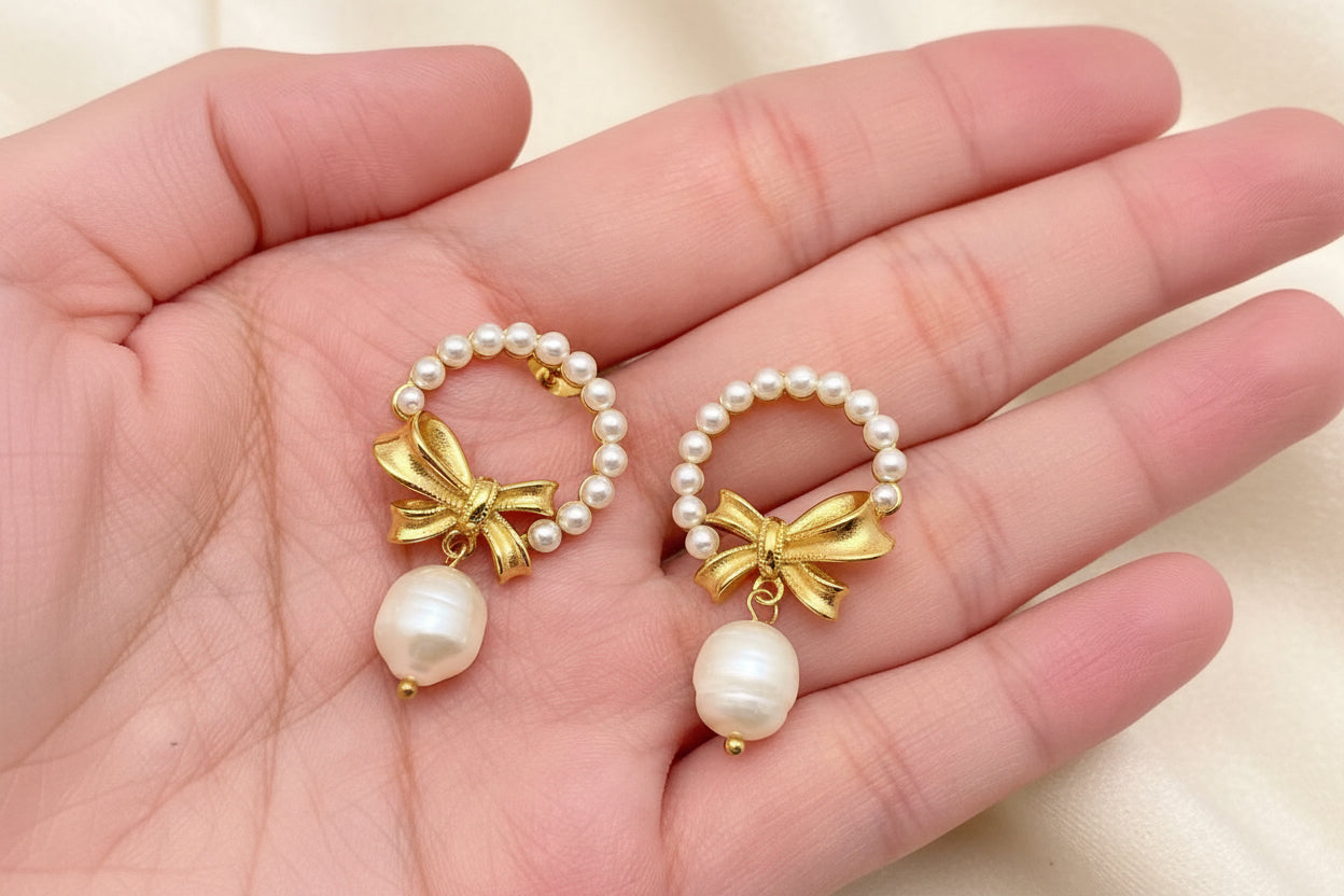 Gold bow and pearl wreath earrings with pearl drops held in a hand