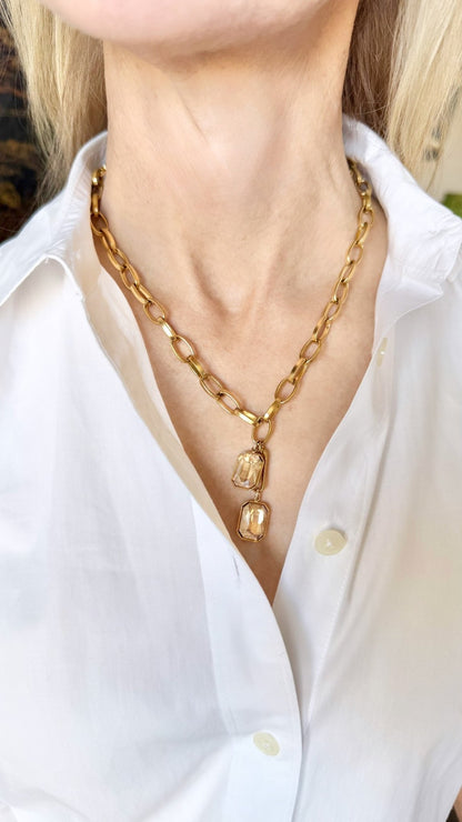 Gold chain necklace with champagne crystal pendant worn by a person in a white shirt