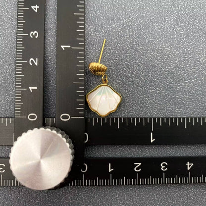one gold shell charm drop earrings with white resin etched shell design laying next to a black ruler and grey background