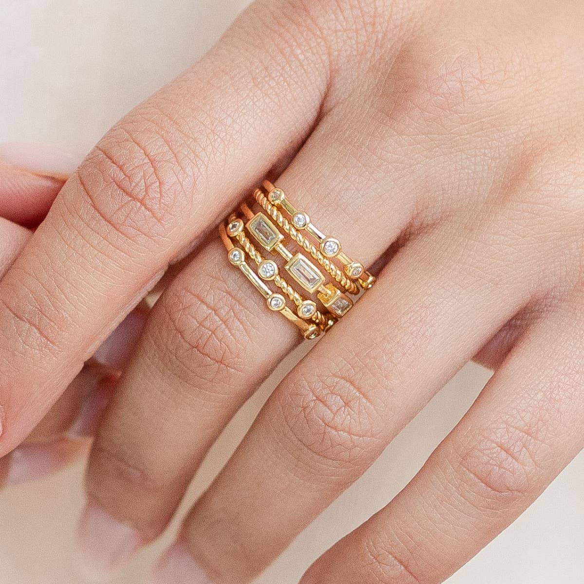 Up close view of a gold ring with embedded stones on a hand against a neutral background