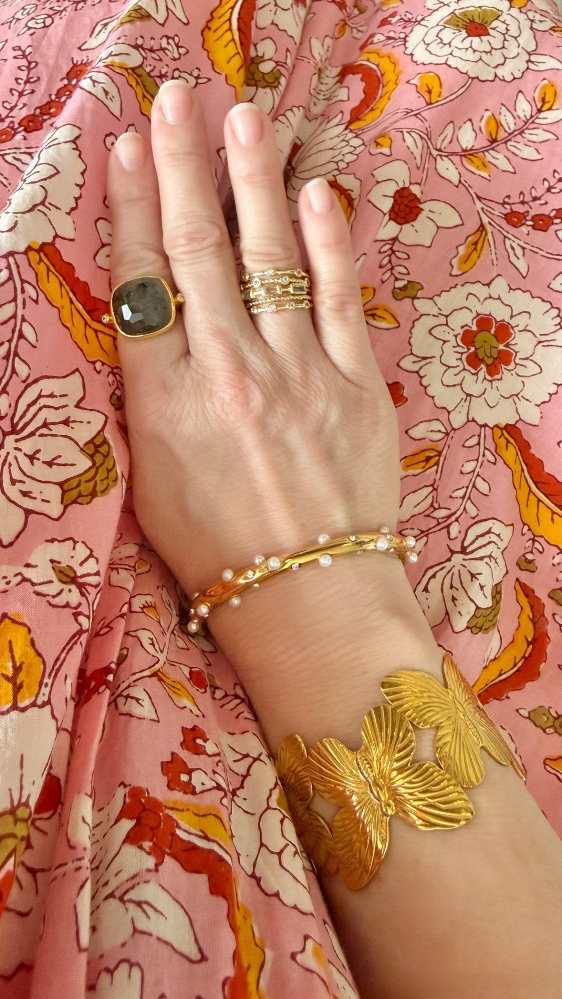 Hand with gold ring and bracelet on a floral pink fabric background