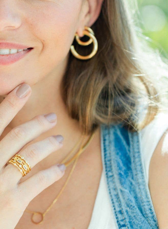 Woman wearing gold jewelry outdoors with a blurred green background