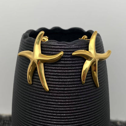 a pair of gold starfish stud earrings hanging on a black vase