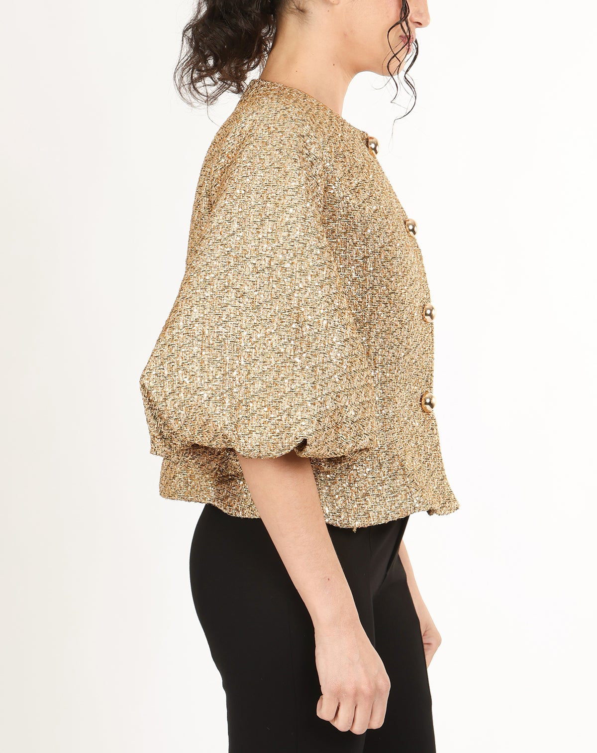 Woman wearing a gold tweed puff sleeve jacket with black pants on a white background