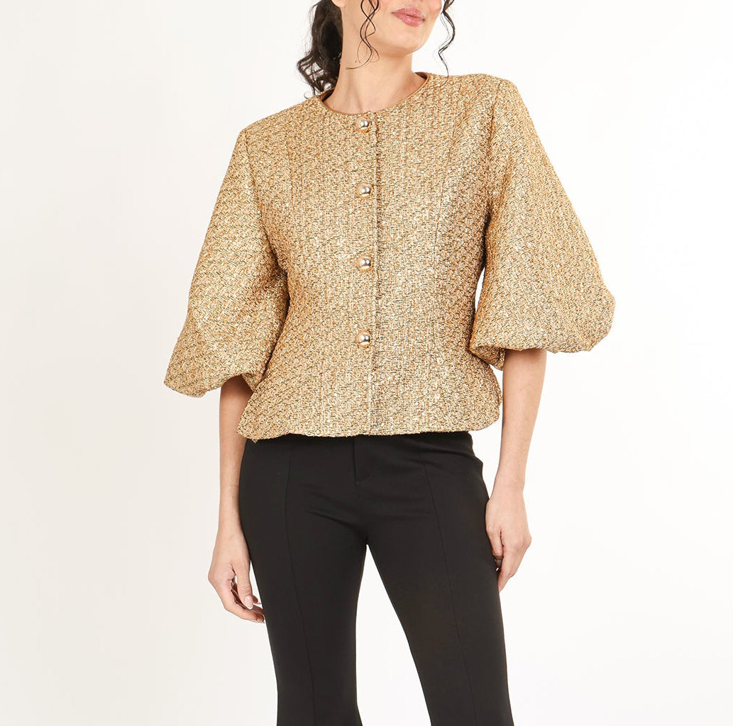 Woman wearing a gold tweed puff sleave jacket with black pants on a white background