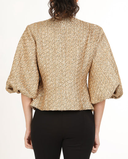 Back view of woman wearing a gold tweed puff sleeve jacket with black pants on a white background