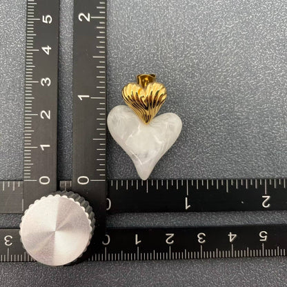 a single gold and white resin heart shaped earring next to a black ruler and a grey background