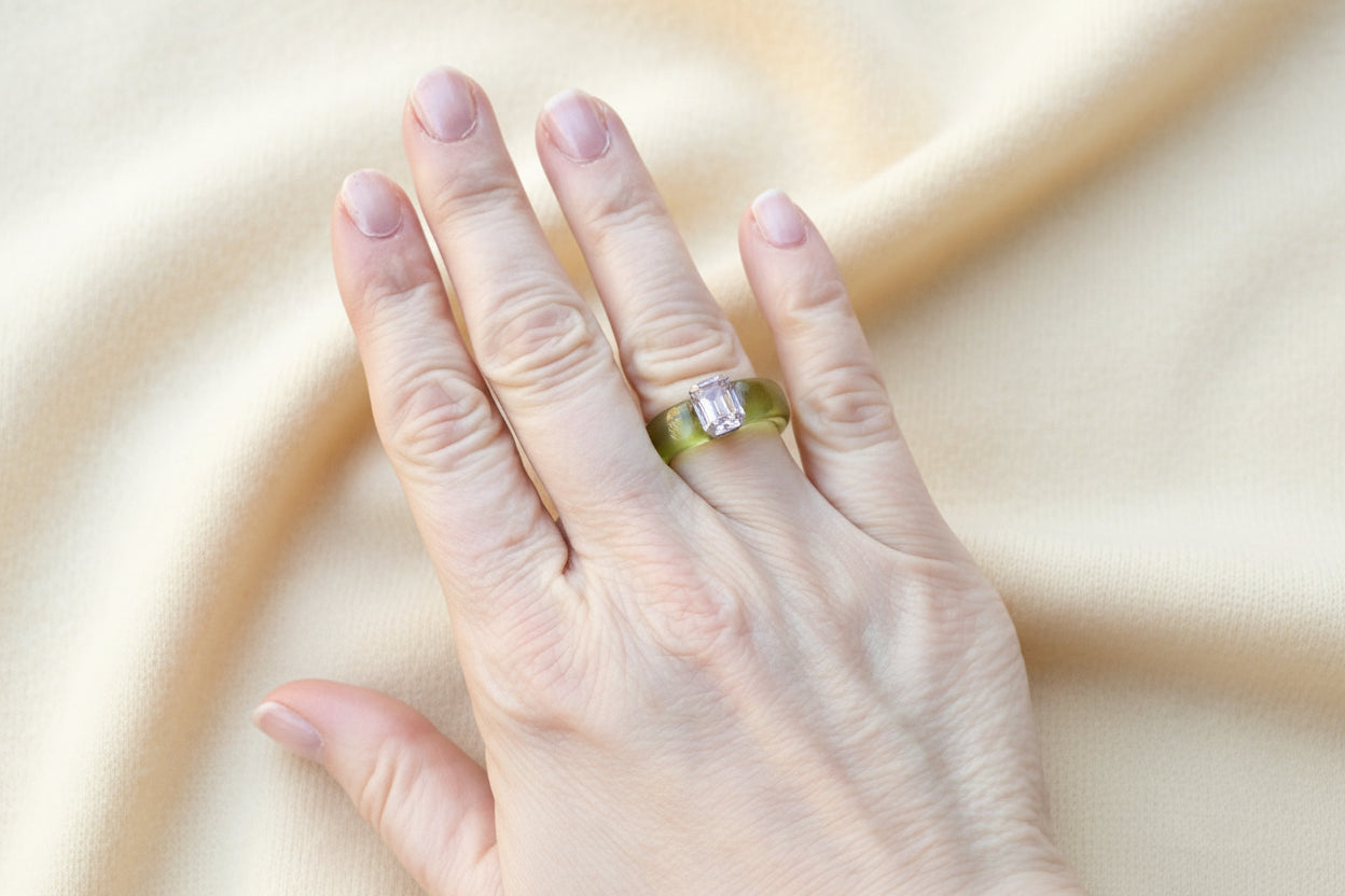 Hand wearing a green acrylic ring with an ivory fabric background