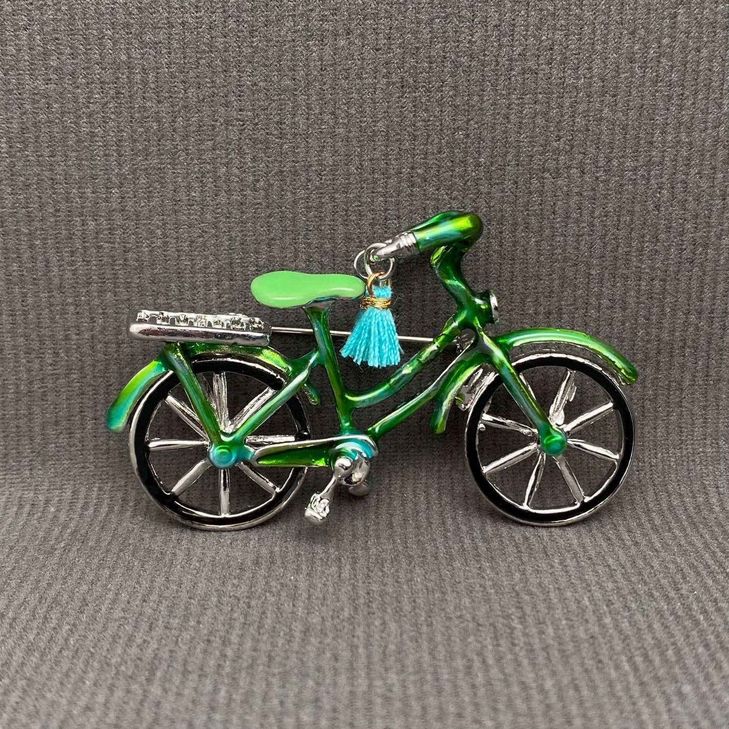 Green bicycle-shaped brooch with a blue tassel on a gray background