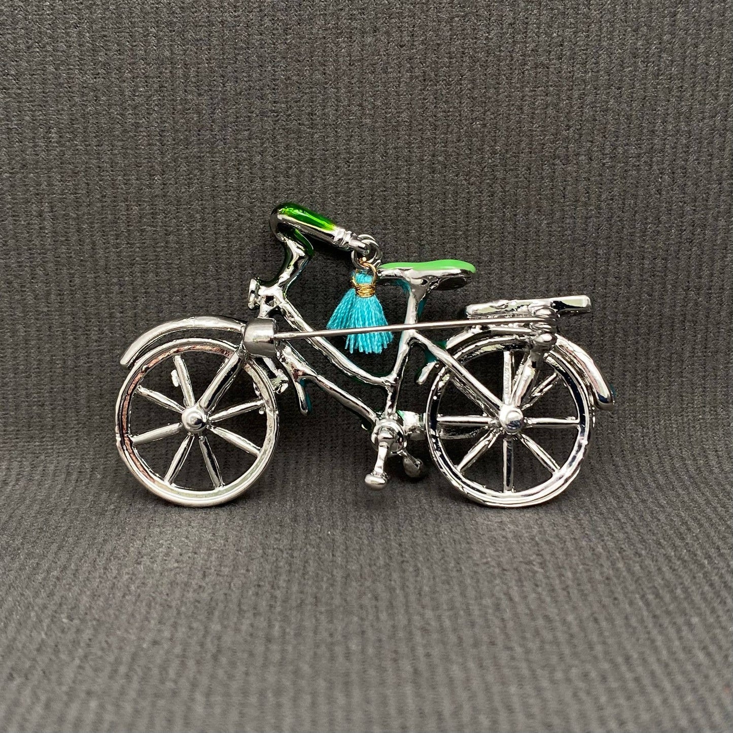 back view of bicycle charm with a green seat and blue tassel on a gray background