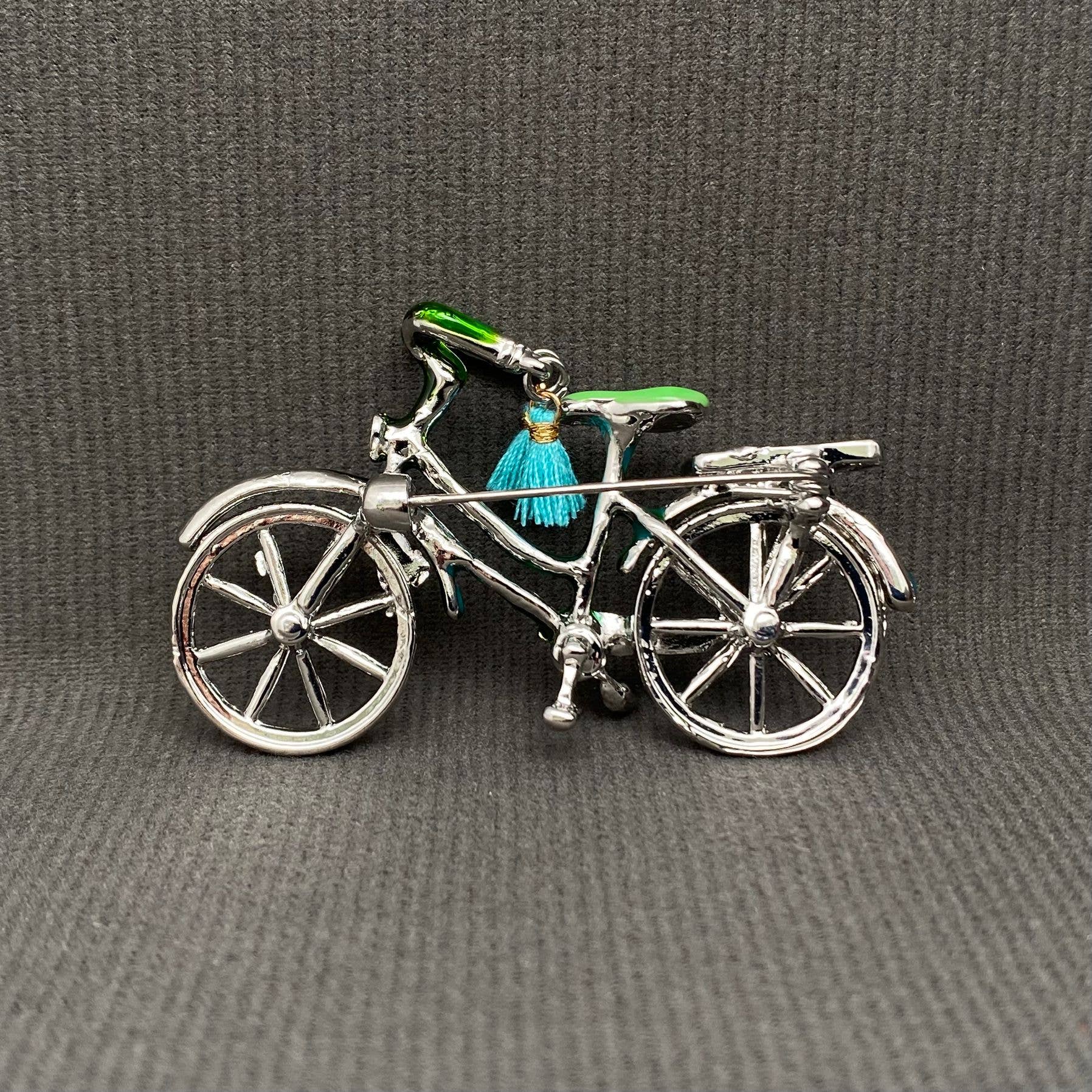 back view of bicycle charm with a green seat and blue tassel on a gray background