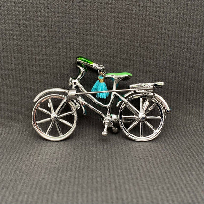 back view of bicycle charm with a green seat and blue tassel on a gray background