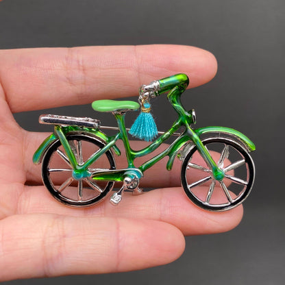 Small green bicycle brooch held in a hand against a dark background