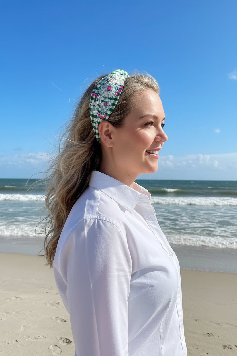 Woman on a beach wearing a floral headband and white shirt with ocean and blue sky in the background