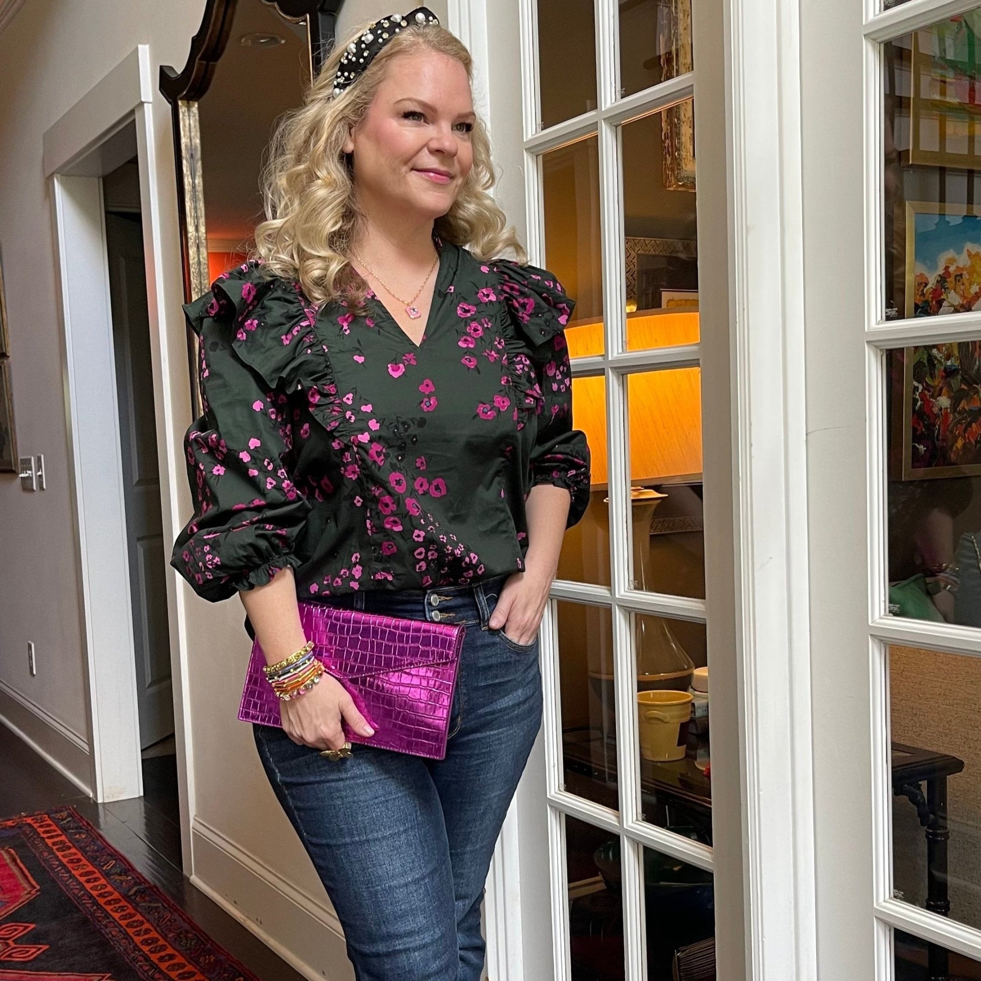 Woman wearing dark floral ruffle top with balloon sleeves and jeans in an indoor setting