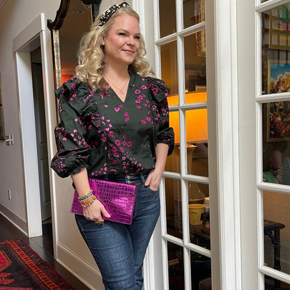 Woman wearing dark floral ruffle top with balloon sleeves and jeans in an indoor setting