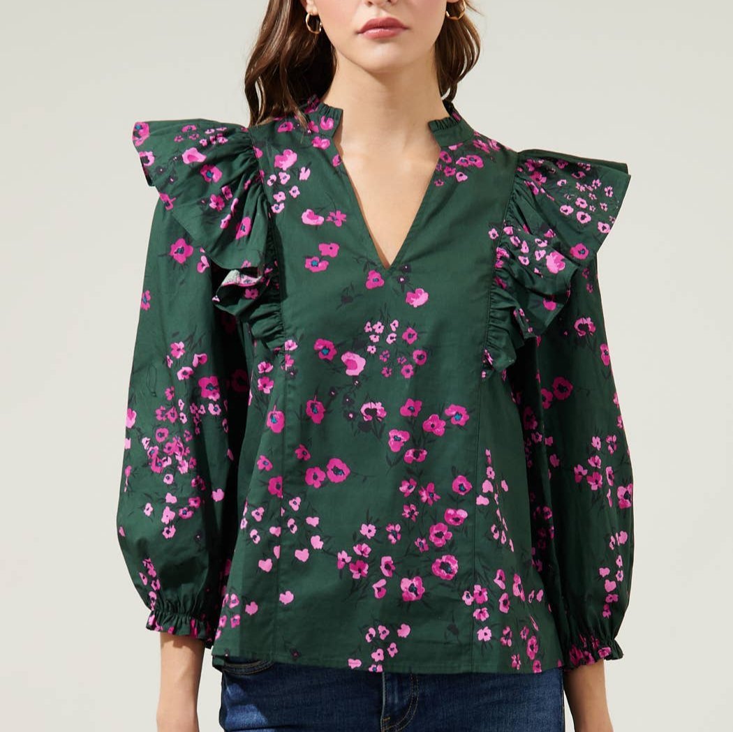 Woman wearing dark floral ruffle top with balloon sleeves and jeans in front of a white background