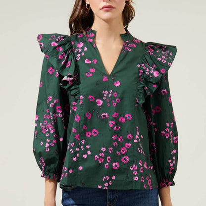 Woman wearing dark floral ruffle top with balloon sleeves and jeans in front of a white background