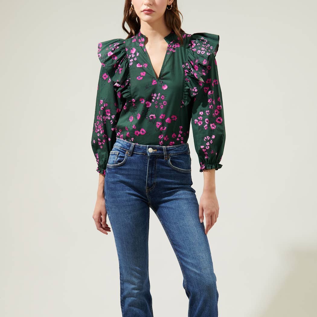 Woman wearing dark floral ruffle top with balloon sleeves and jeans against a white background