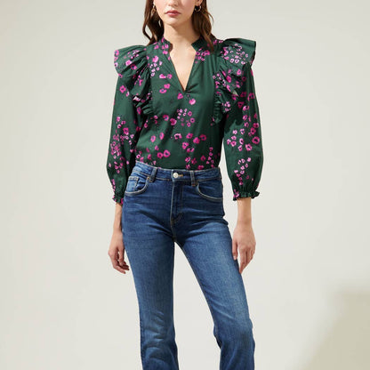 Woman wearing dark floral ruffle top with balloon sleeves and jeans against a white background