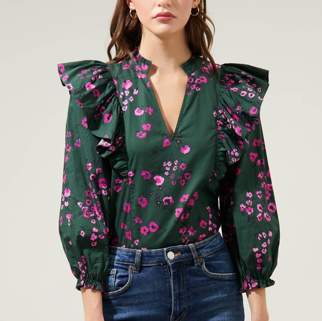 Woman wearing dark floral ruffle top with balloon sleeves and jeans in front of a white background