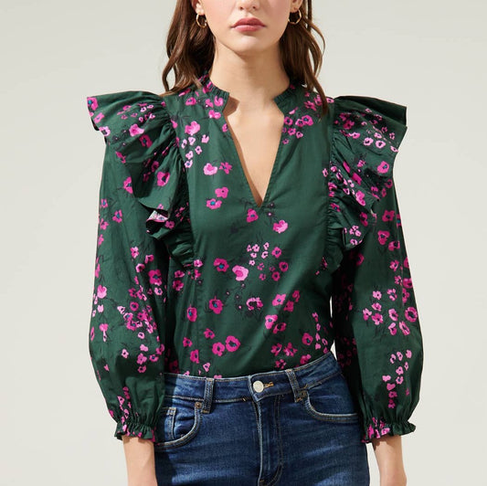 Woman wearing dark floral ruffle top with balloon sleeves and jeans in front of a white background