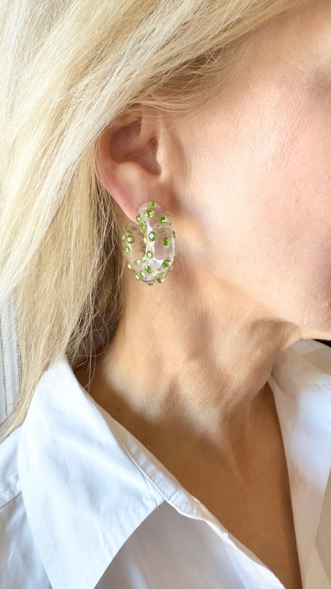 Close-up of a person wearing a hoop earring with green stones.