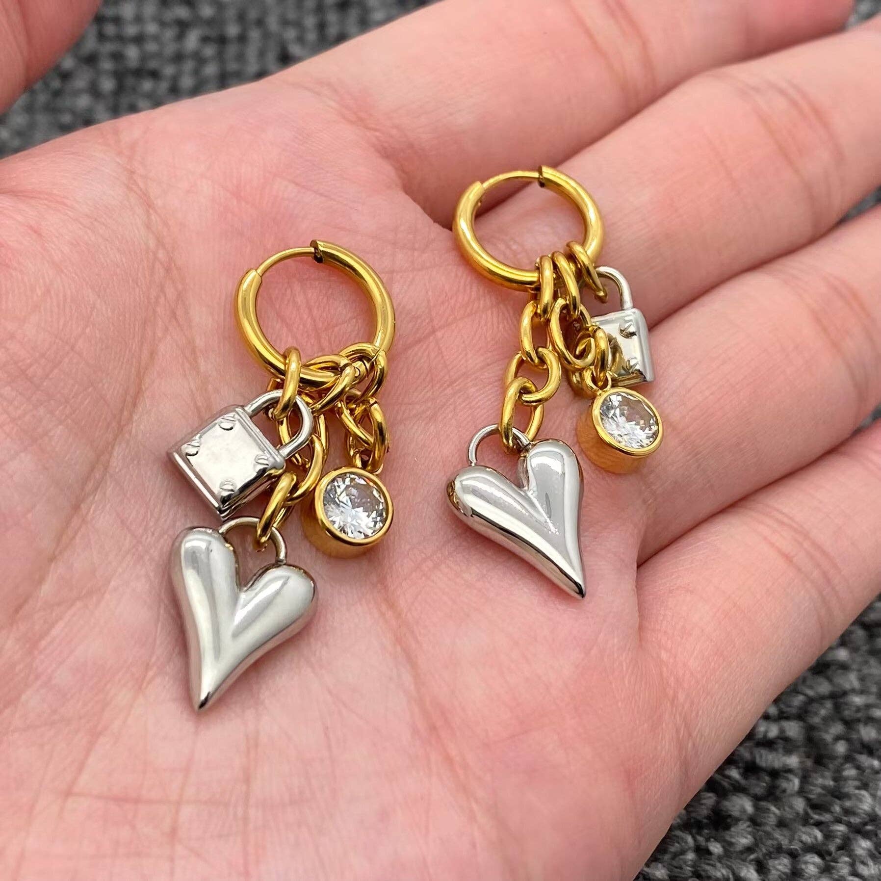 Gold and silver heart-shaped earrings with charms on a hand.
