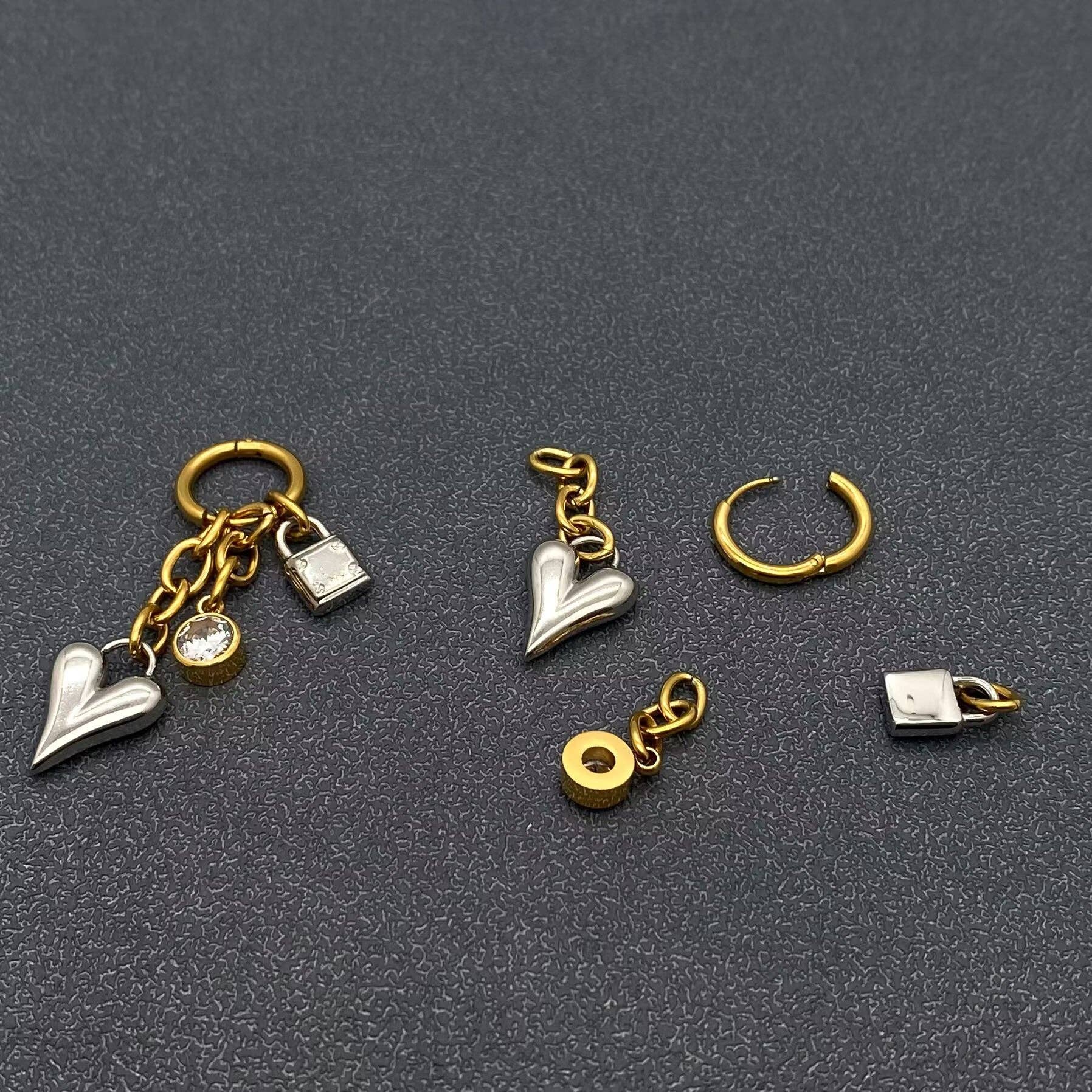 gold and silver heart, lock, and crystal charm earrings on a dark grey background