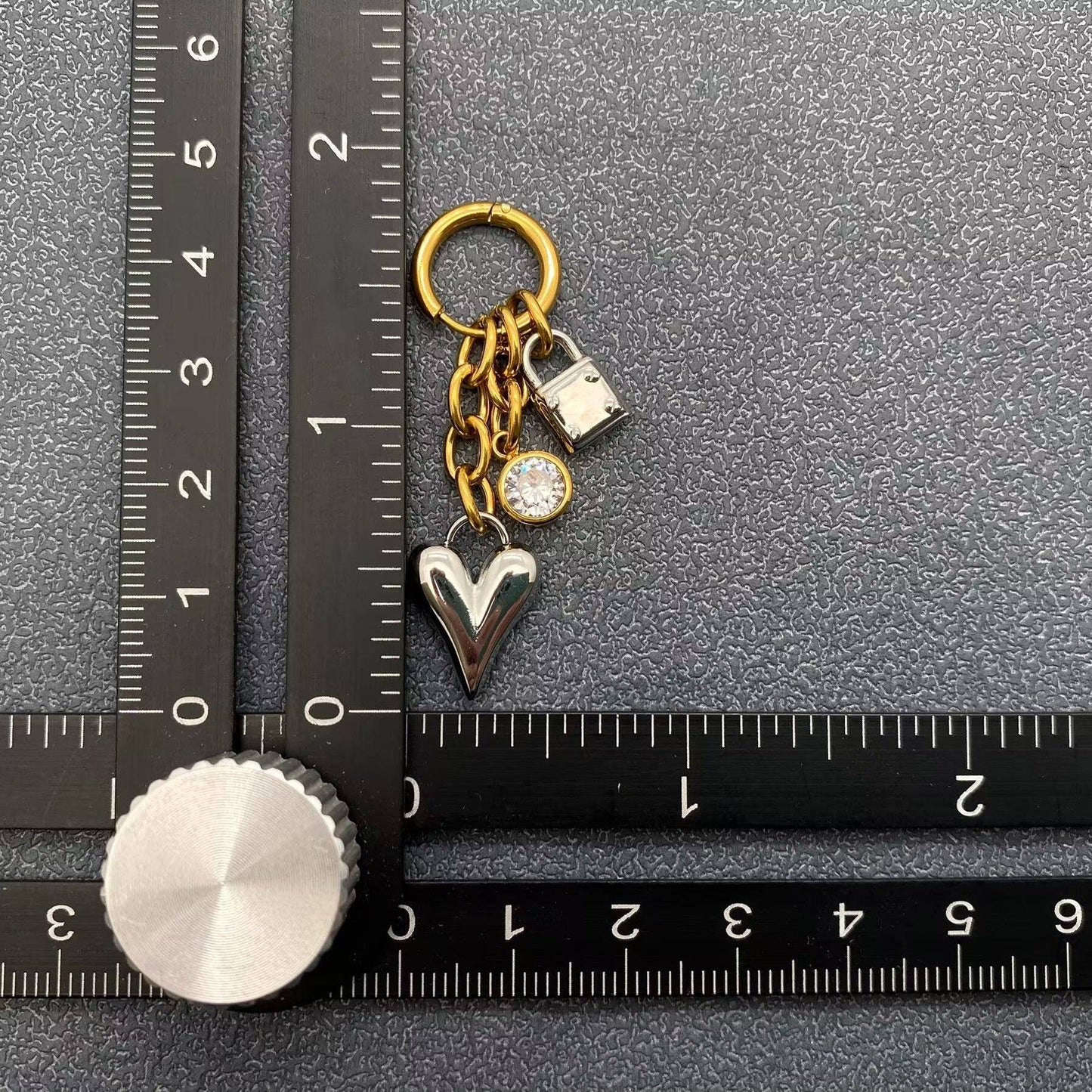 Earring with heart and lock charms next to a ruler on a textured surface