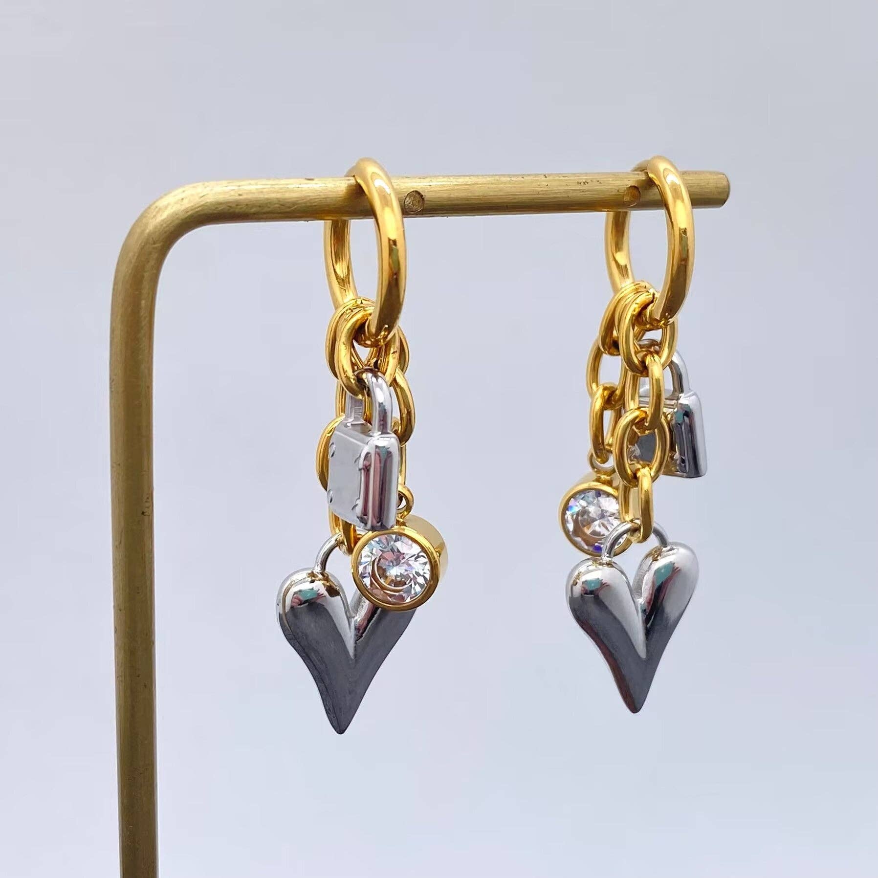 Gold and silver heart-shaped earrings on a stand against a light gray background