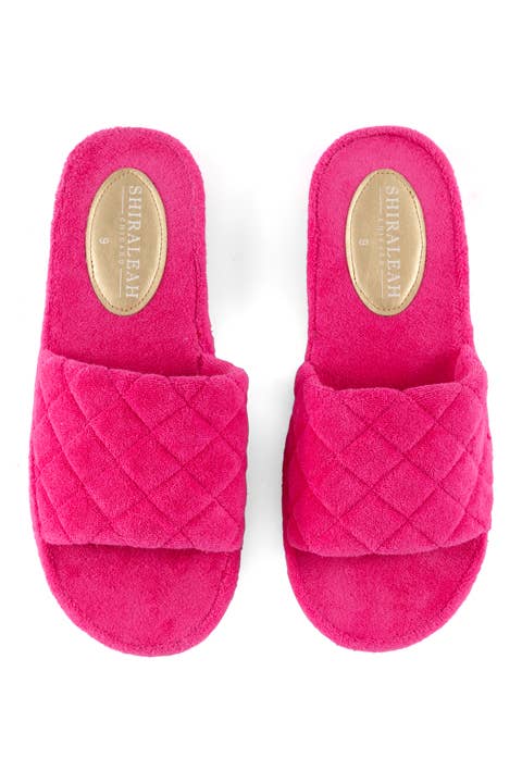 A pair of pink terrycloth pool slides with a diamond pattern on the straps and a flat rubber-like sole against a white background
