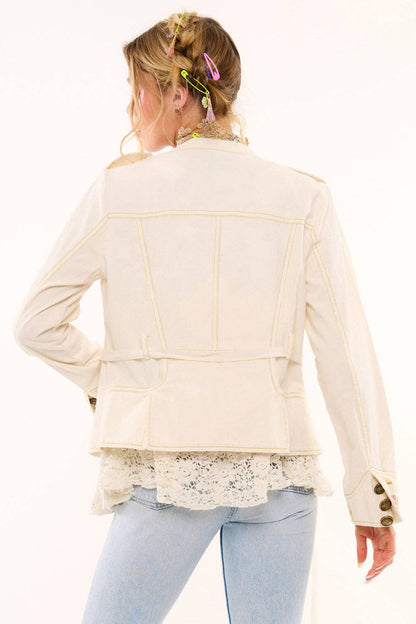 Woman wearing a cream-colored jacket with lace details on a white background