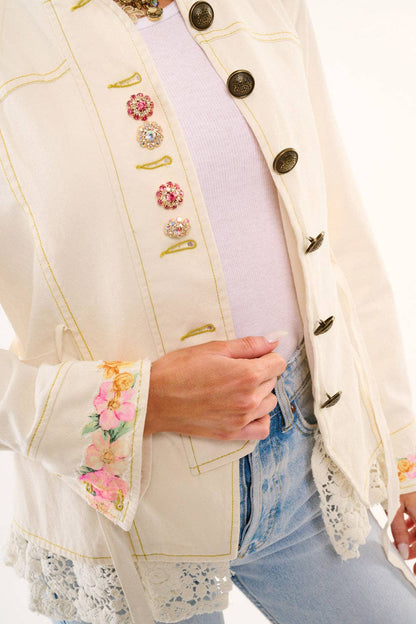Close-up of a person wearing a decorative white jacket with floral embroidery and buttons.