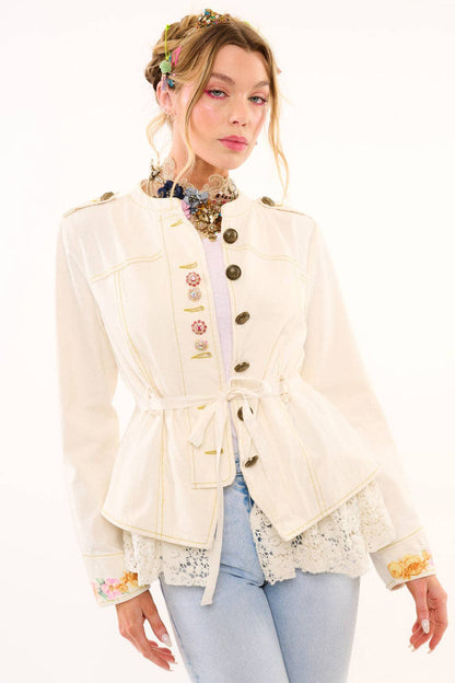 Woman wearing a cream-colored jacket with floral details on a white background