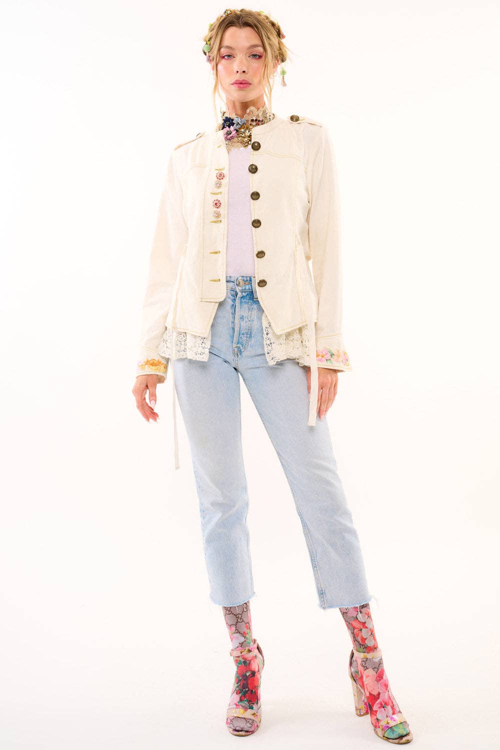 Woman wearing a cream jacket, light blue jeans, and floral shoes on a white background