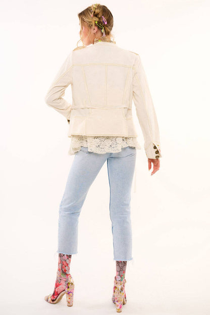 Woman wearing a cream jacket, light blue jeans, and floral shoes on a white background