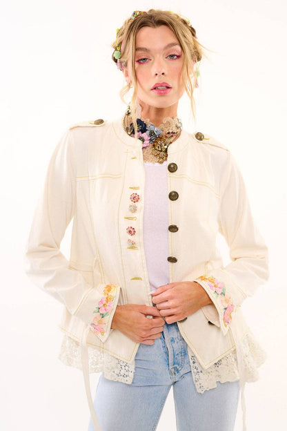 Woman wearing a decorative cream-colored jacket with floral accents on a white background