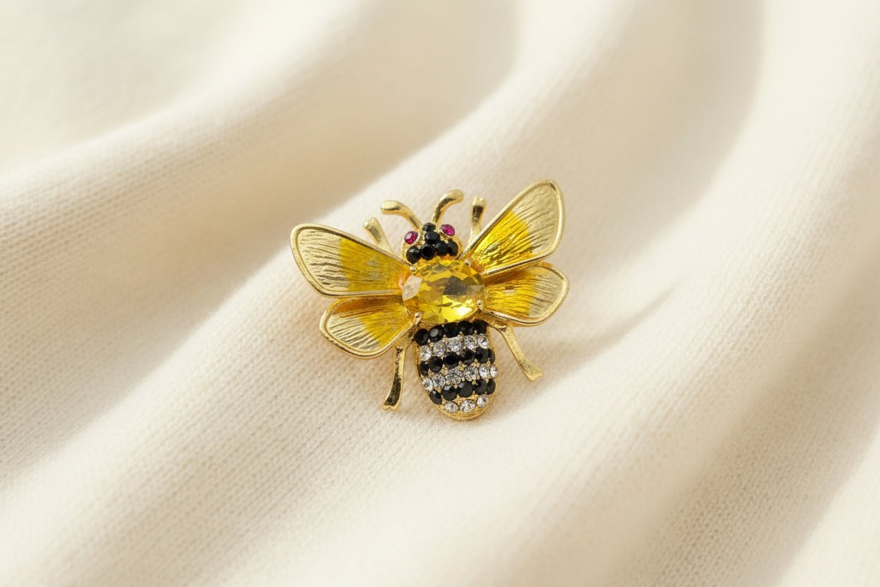 Gold bee-shaped brooch with gemstones on an ivory fabric background