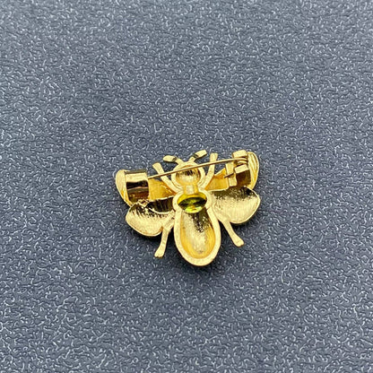 Back view of gold bee-shaped brooch to show pin closure on a textured gray background