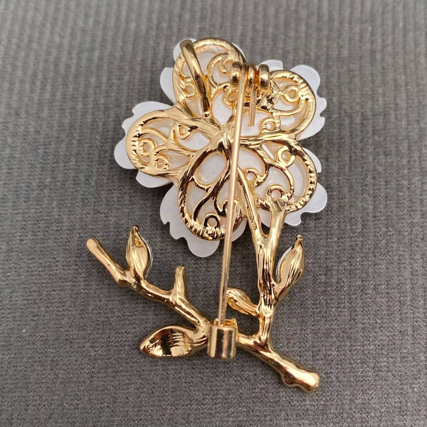Back view of white flower and gold brooch to show pin closure on a gray background