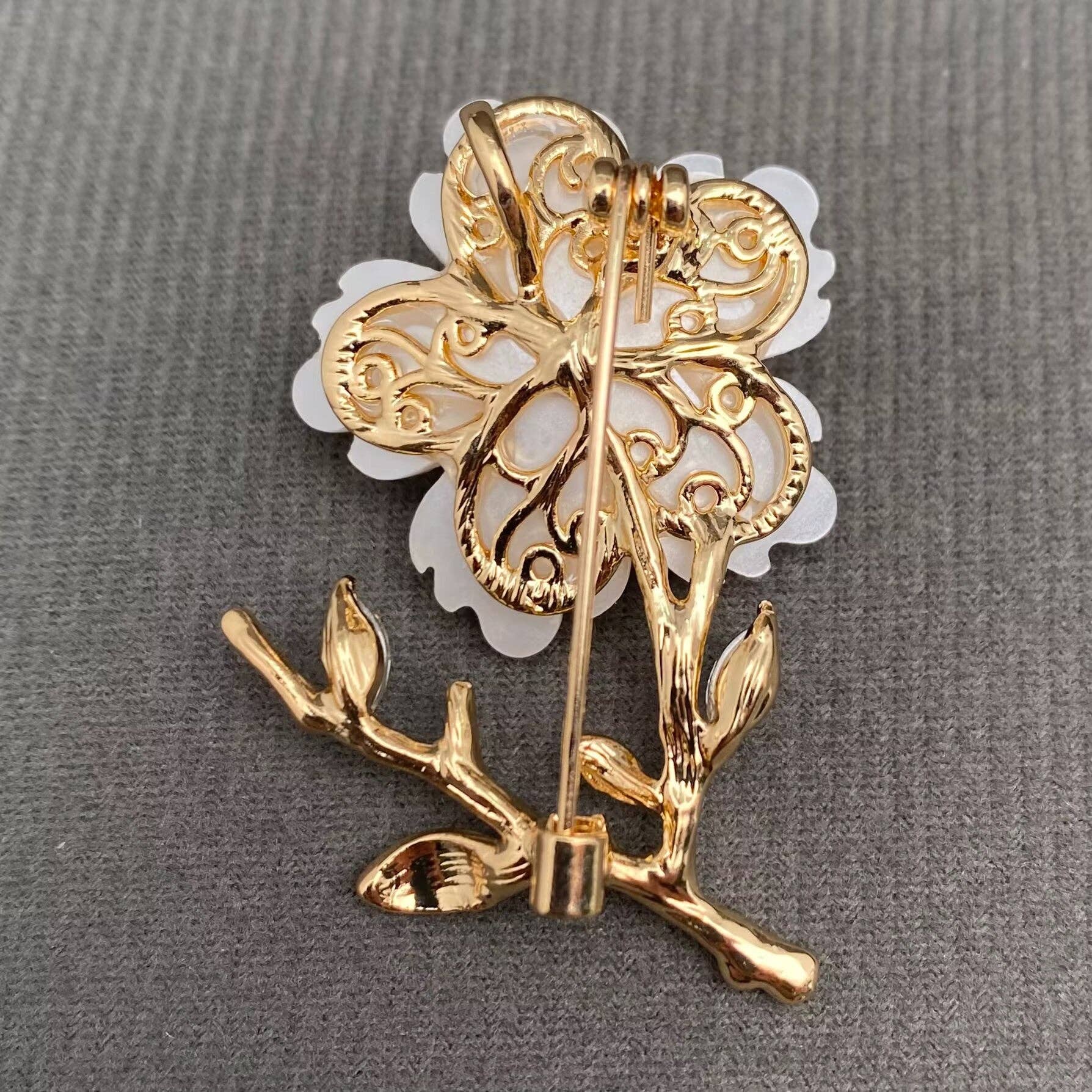 Back view of white flower and gold brooch to show pin closure on a gray background