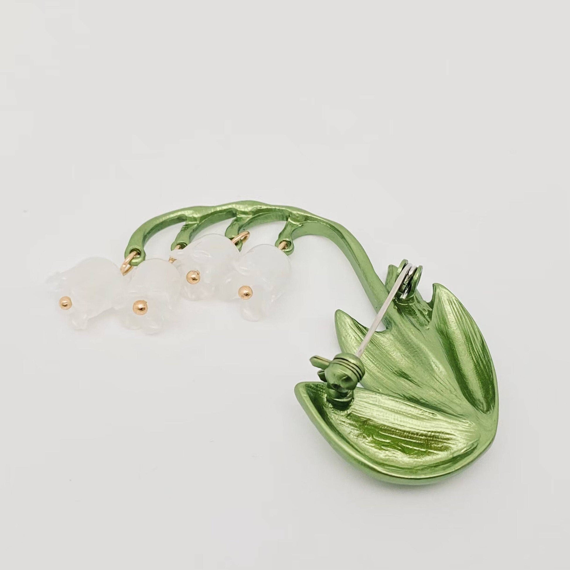 Back view of a green and white Lily of the Valley brooch to show the pin closure on a light gray background