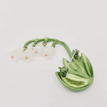Back view of a green and white Lily of the Valley brooch to show the pin closure on a light gray background