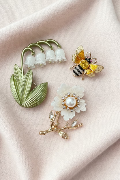two floral brooches and 1 bee brooch against a pale pink fabric background